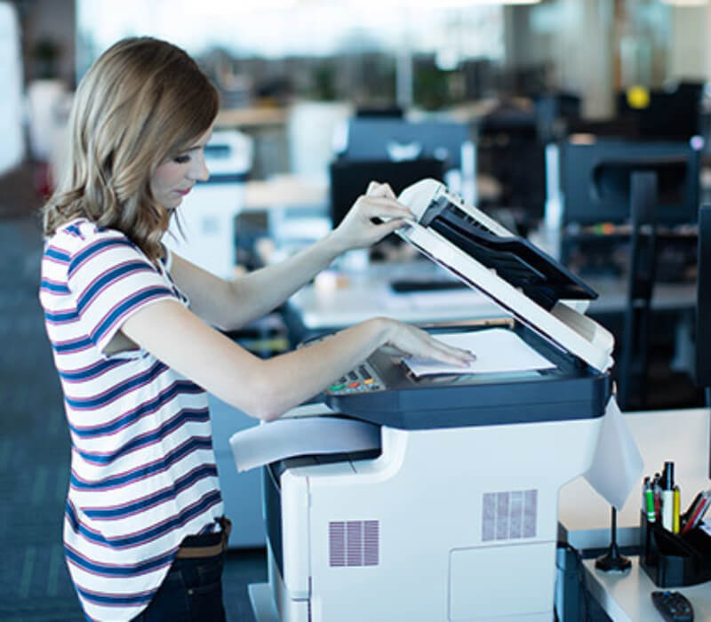 Young female standing at an office copier, with the top open putting a piece of paper on the glass scanner